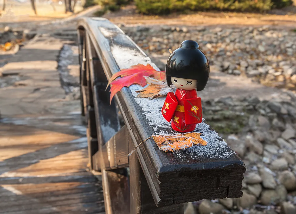 Japanese wooden doll Kokeshi on the background of maple leaves with frost. Concept season maple leaves Momiji-gari.